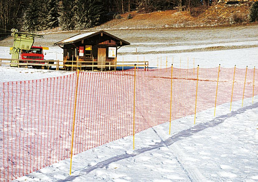 Ski-slope net, orange, on snow with little house in the back, outside picture