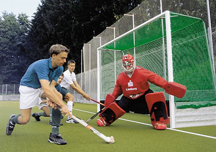 Field hockey goal net, green, front view, with players and goal keeper, outdoors
