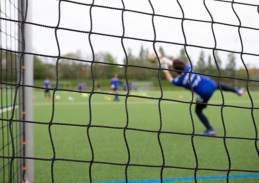 Goal keeper kid jumping for the ball, view from behind the goal net