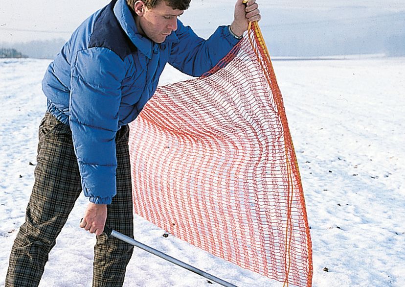 Man pulling out ground sleeve for ski-slope barrier net, outside picture (in snow).
