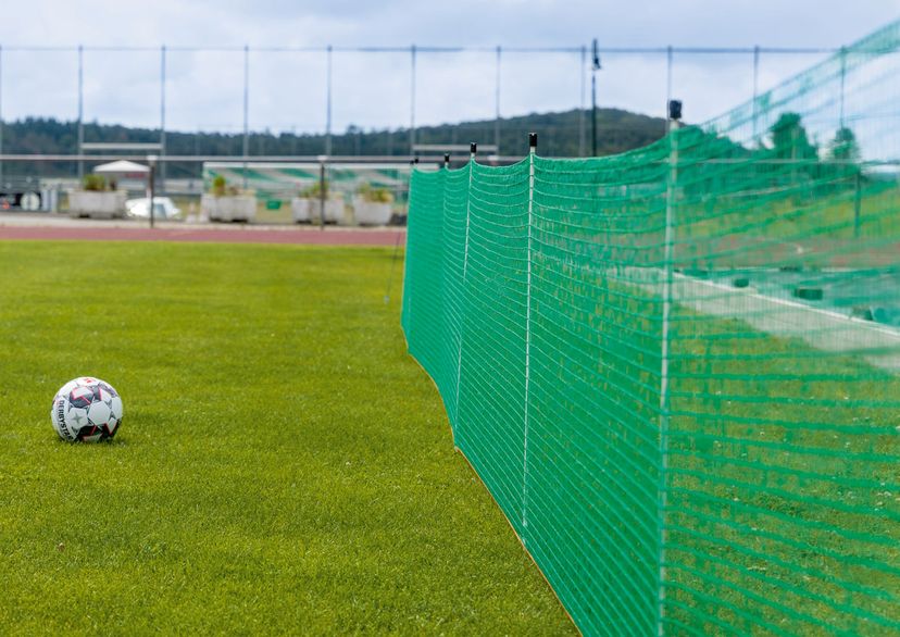 Green barrier fence in a sport stadium with a ball laying beside it, outside picture.