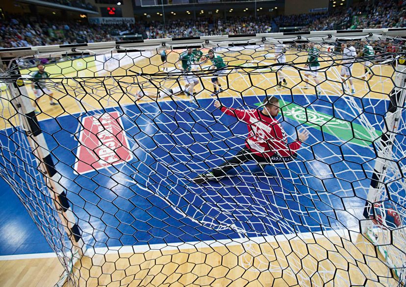 Goal keeper in front of handball goal with ball flying into the net