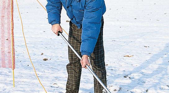 Man with blue jacket builds up snow fence, red, in snow, outside picture