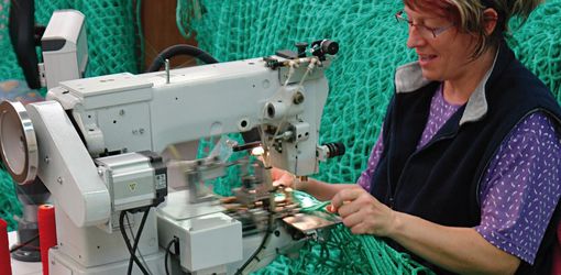 Frau an einer Nähmaschine arbeitet an einem grünen Netz