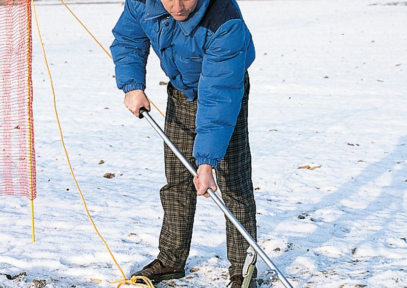 Man with blue jacket builds up snow fence, red, in snow, outside picture