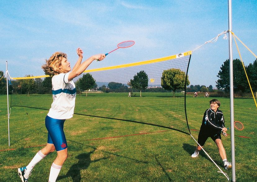 Badminton Net for leisure, with yellow headband, 2 female players, action scene, one jumping to hit the ball with racket, playing on green gras, outdoors