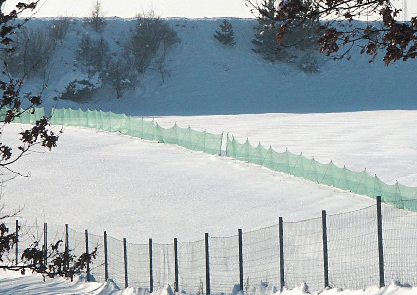 Schneefangzaun, grün, mit Schnee und Berg im Hintergrund