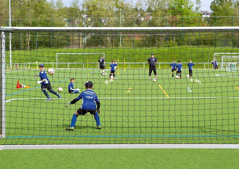 Kids football training with coach, view from the back of the goal net