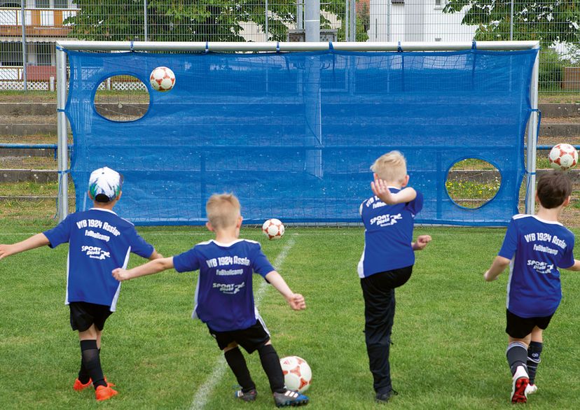 Torschussübungswand in blau mir 4 Jugendspielern, die auf das Tor Bälle schießen