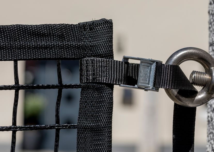 Area confinement net in black with buckled strap fastened to a screw bolted into a wal, detail picture