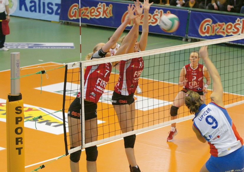 Volleyball tournament net with 2 women blocking and 1 woman waiting behind the net and one woman in front of the net, indoor, action picture