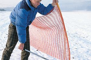 Man pulling out ground sleeve for ski-slope barrier net, outside picture (in snow).