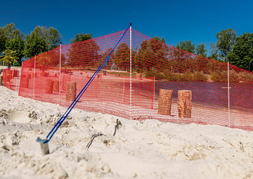 Blaues Spannseil an rotem Begrenzungszaun mit Erdanker im Sand
