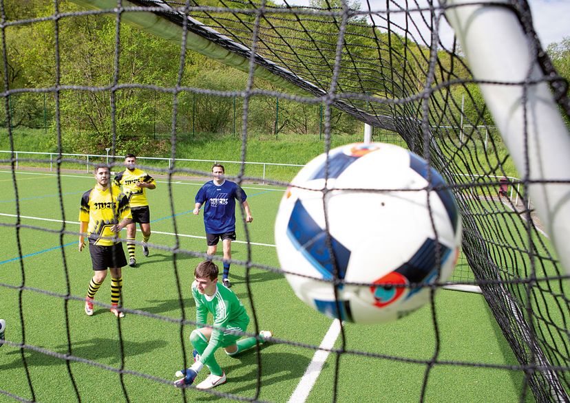 Ball der in Ultra Fußballtornetz fliegt mit 5 Spielern im Hintergrund